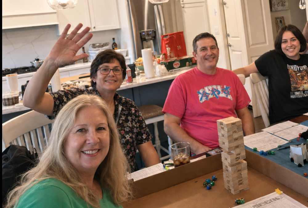 Players smiling at a tabletop session with dice, sheets, and table materials visible.